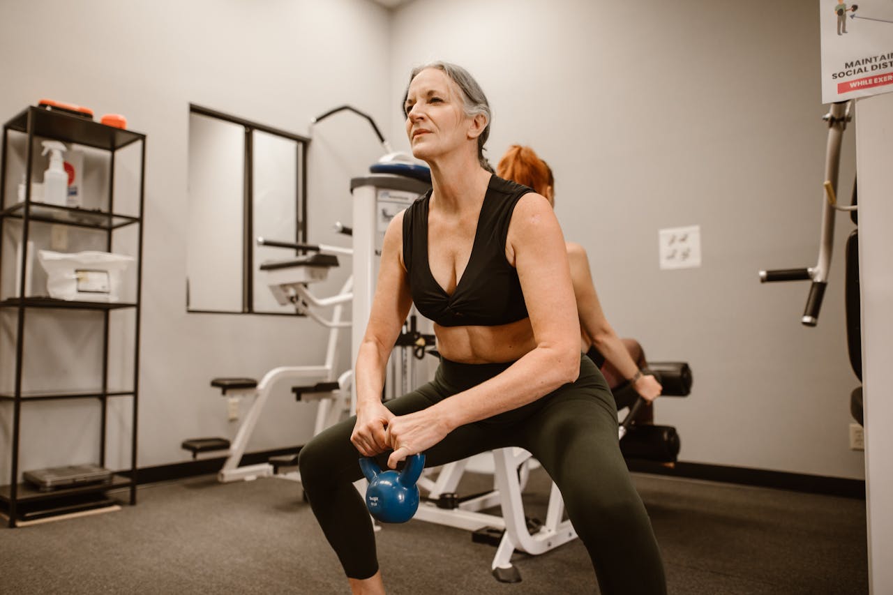 Active senior woman performing kettlebell squats for strength training at indoor gym.