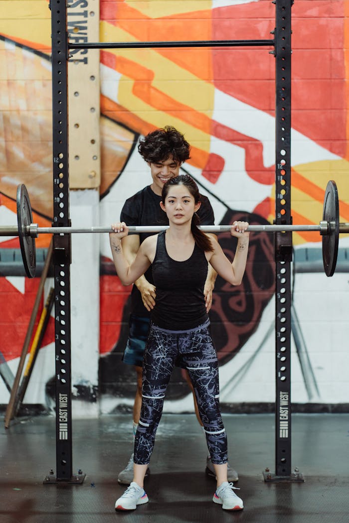 A man and woman engage in weight lifting at a colorful gym, displaying teamwork and strength.